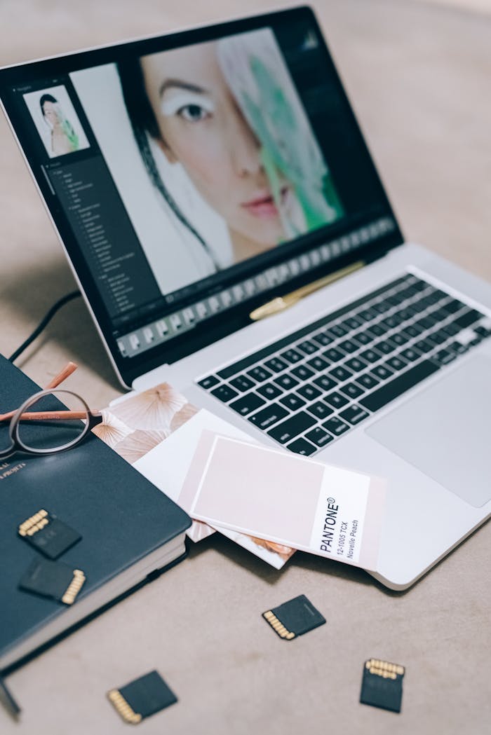 A workspace with a laptop displaying editing software, memory cards, and Pantone color guide.