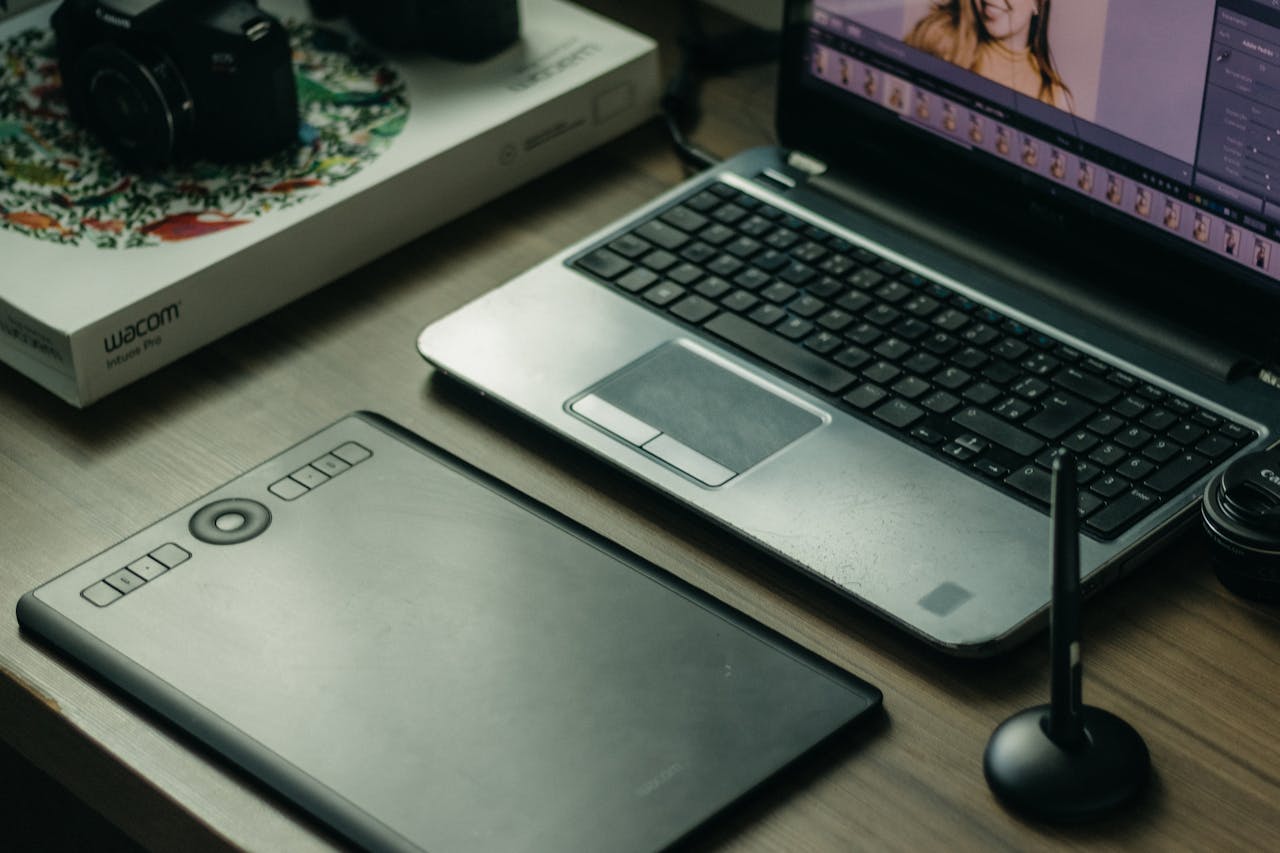 Modern digital artist setup with laptop, tablet, and stylus on desk.